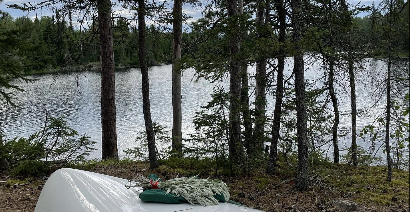 An overturned canoe at the edge of a northern lake holding sage, an abalone shell, and matches prepared for smudge.